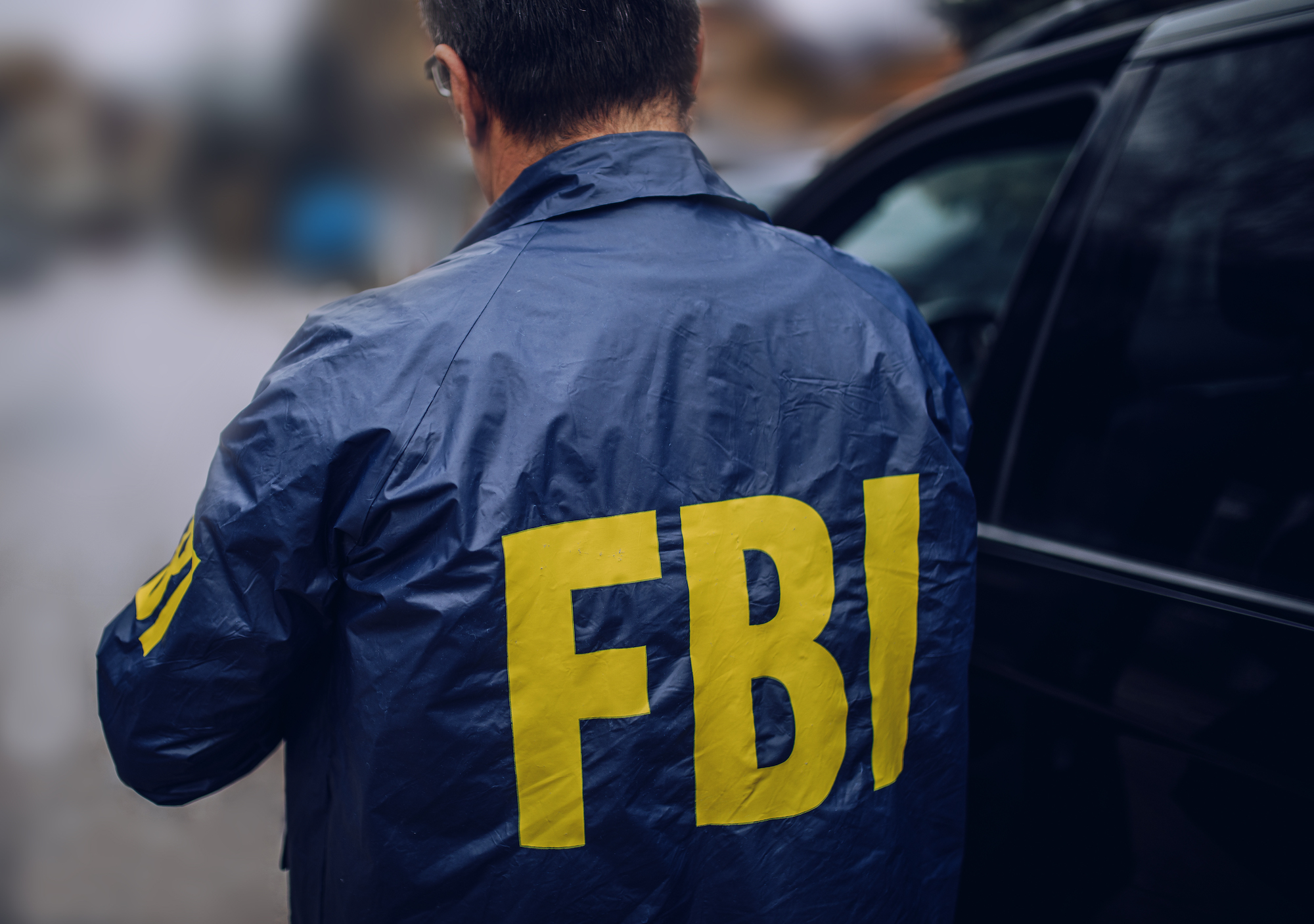 professional in FBI jacket by car