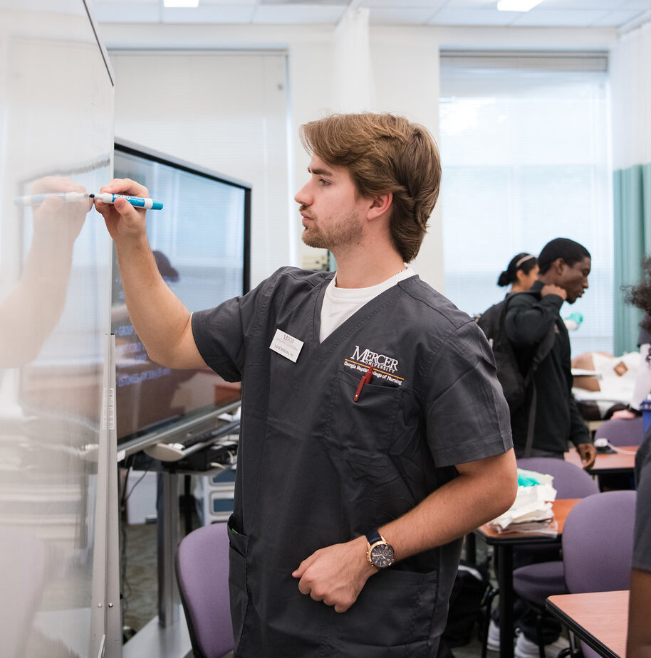 Mercer BSN student in scrubs writing on whiteboard