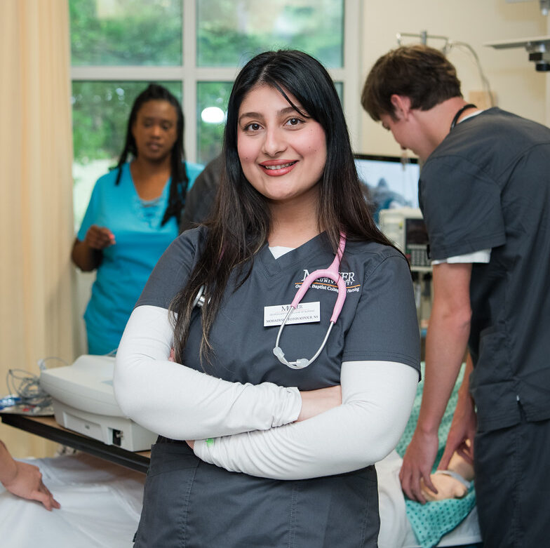 Mercer BSN student in scrubs in nursing lab, facing camera, arms folded and smiling