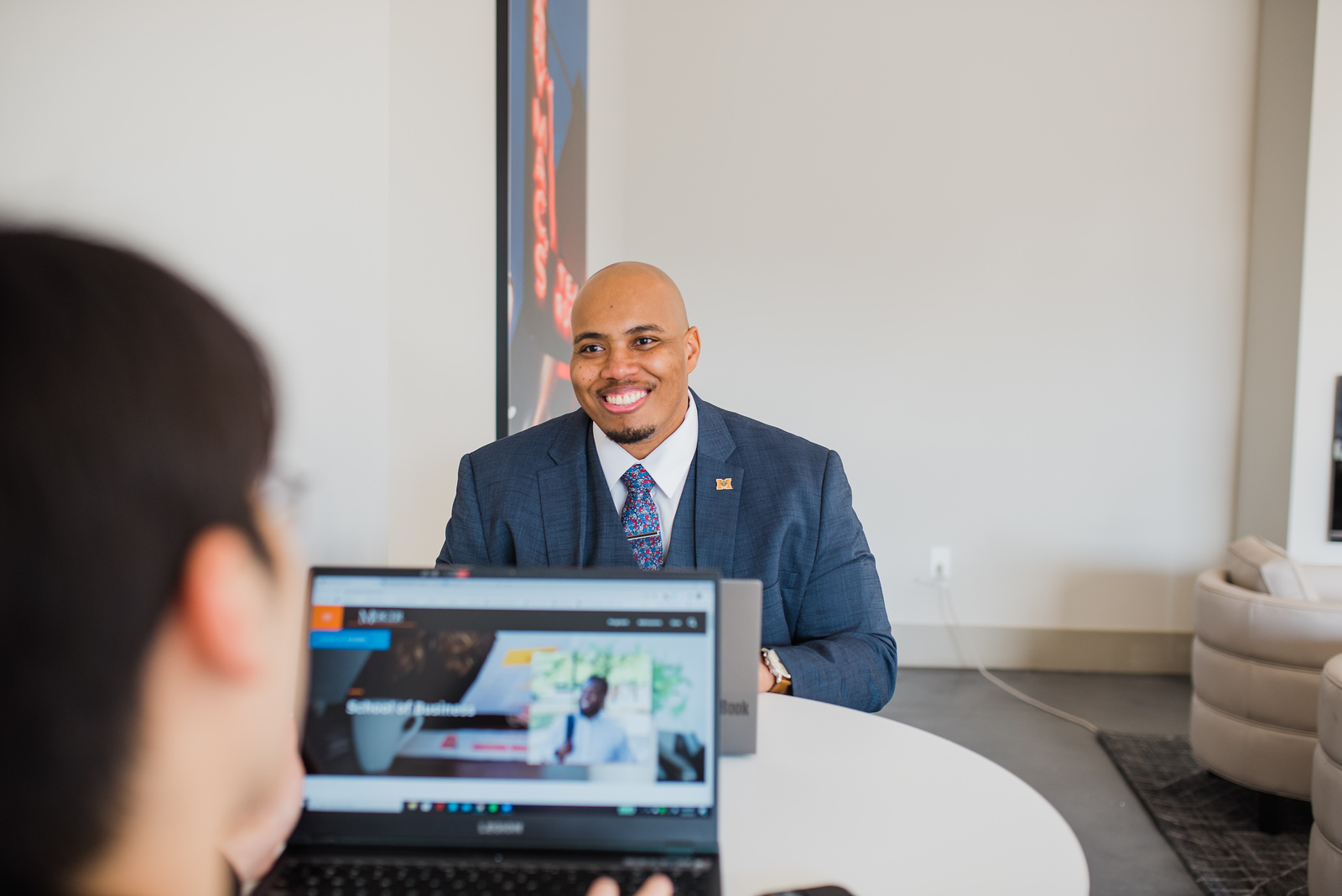 Mercer MBA student in suit sitting across from colleague who has laptop open, smiles