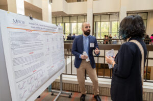pharmacy student presenting his research poster to a woman holding a brochure