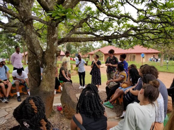 Mercer On Mission in Rwanda; group of counseling students and Rwandans hosting narrative therapy session outdoors. The group is standing in a circle under a tree.
