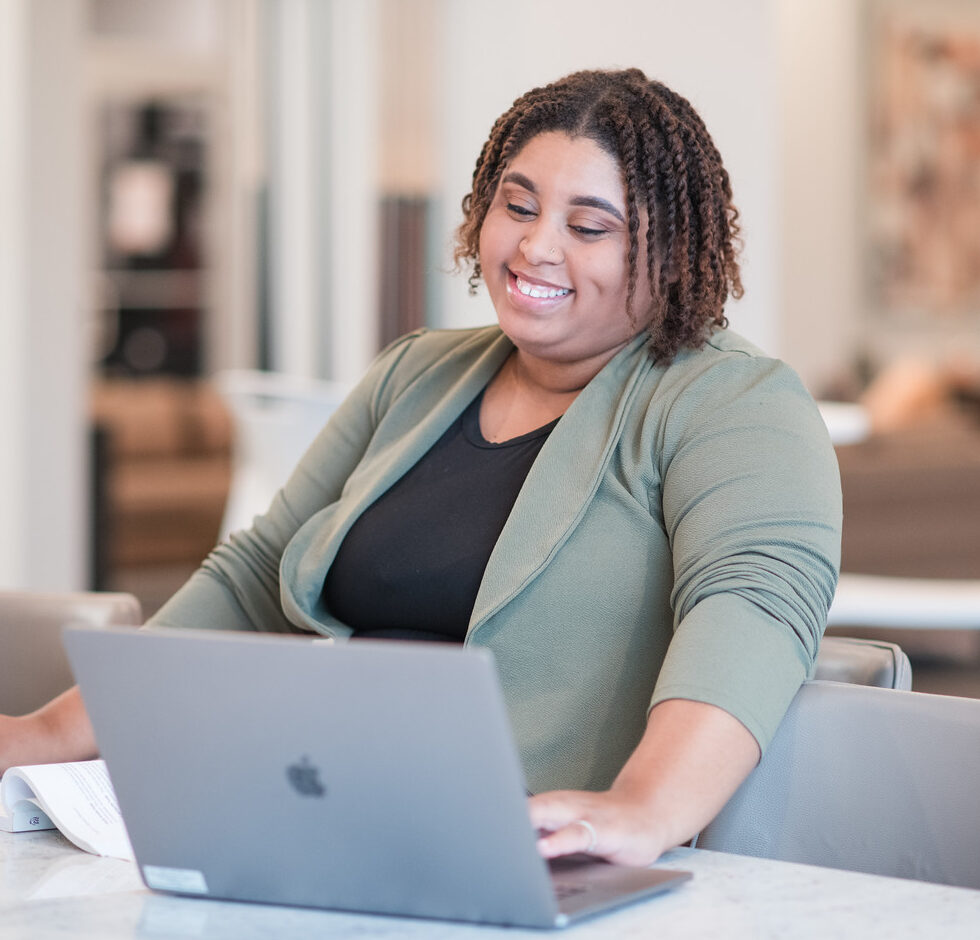 mercer student in green blazer smiling and looking at laptop