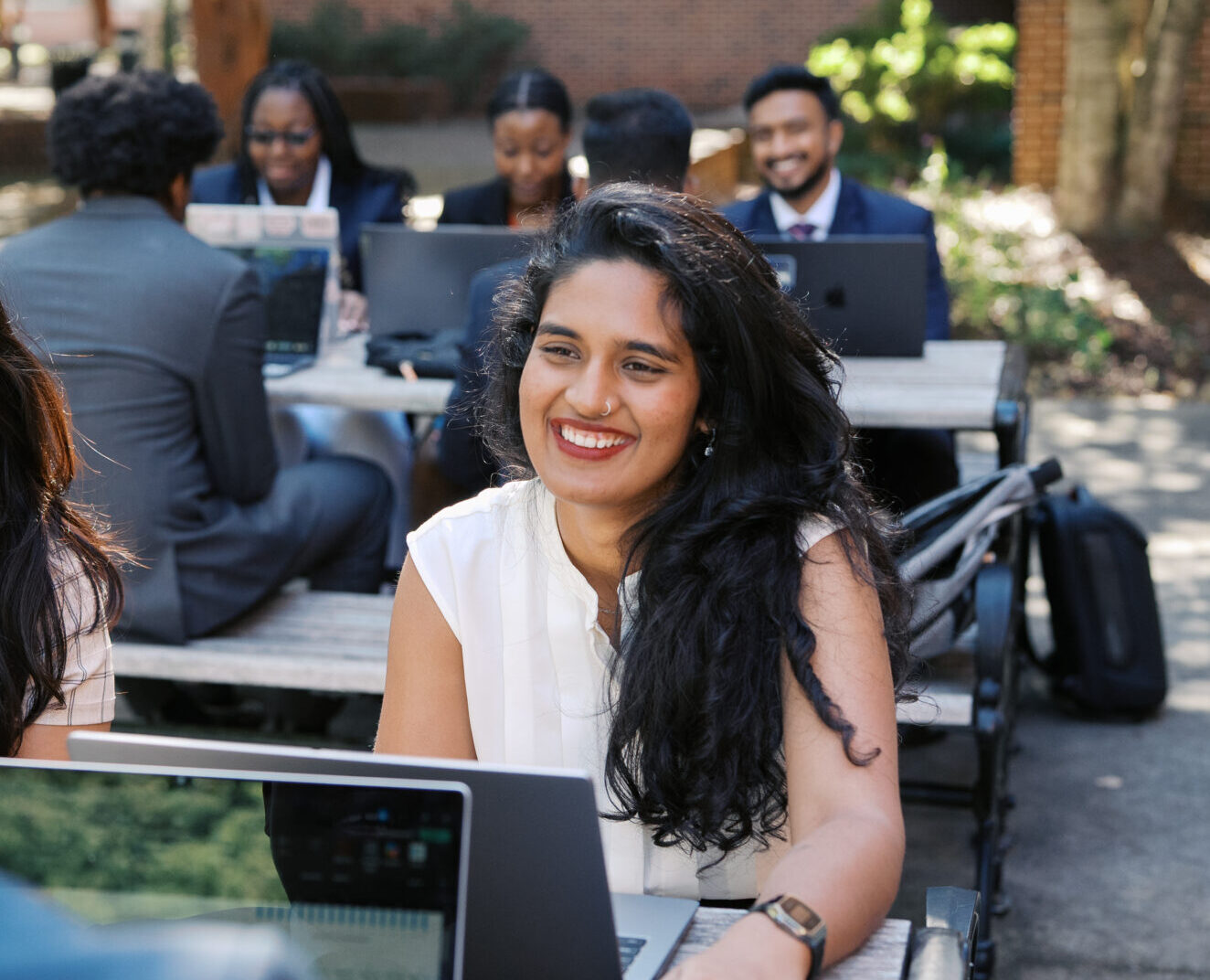 female business student outside at table in business attire smiling, laptop open